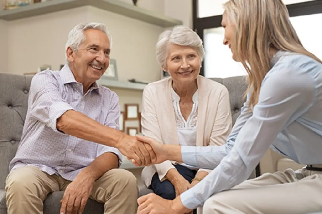 An elderly couple and a professional woman shaking hands while seated in a living room An elderly couple and a professional woman shaking hands while seated in a living room