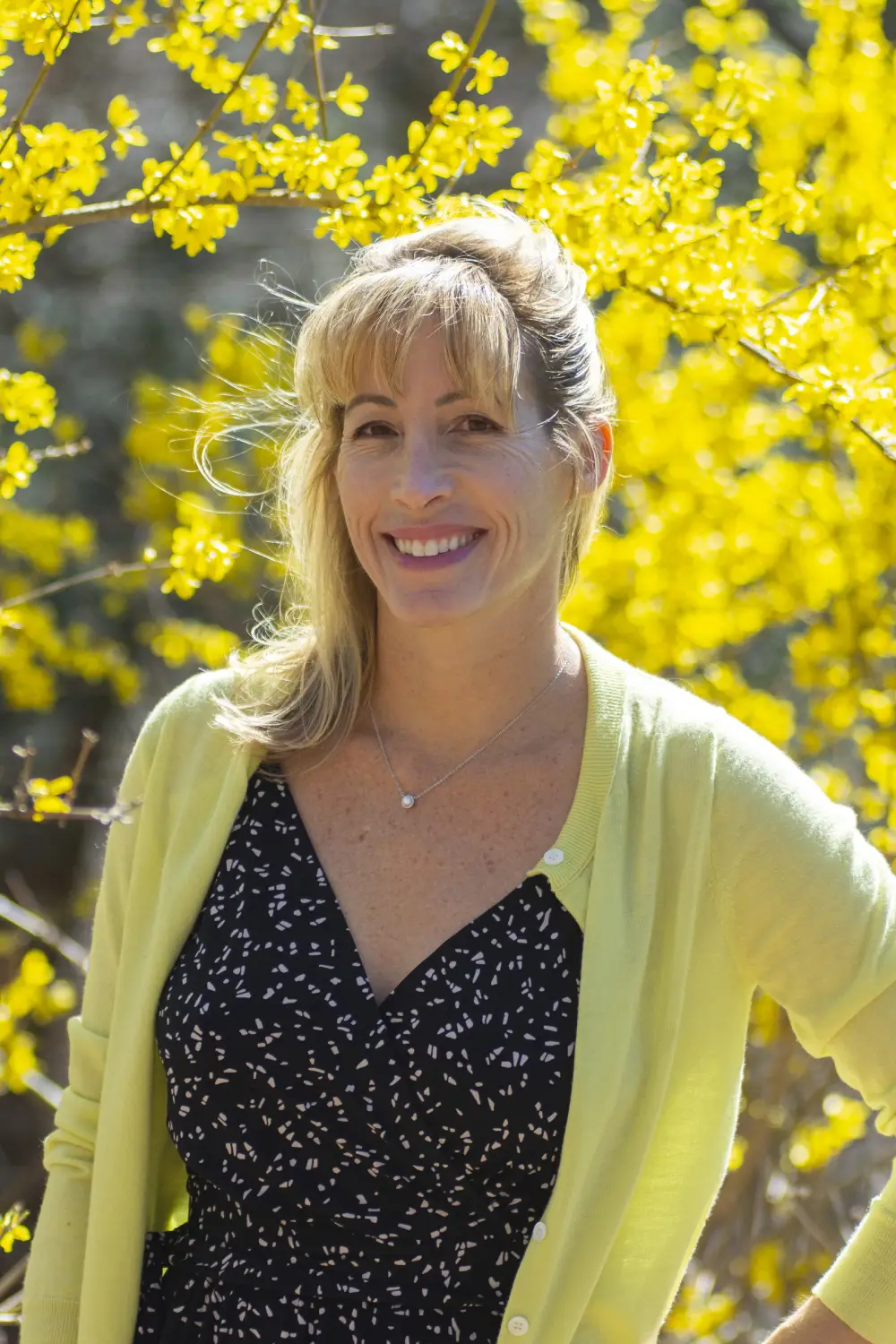 person in a black dress and yellow cardigan with a backdrop of yellow flowers person in a black dress and yellow cardigan with a backdrop of yellow flowers