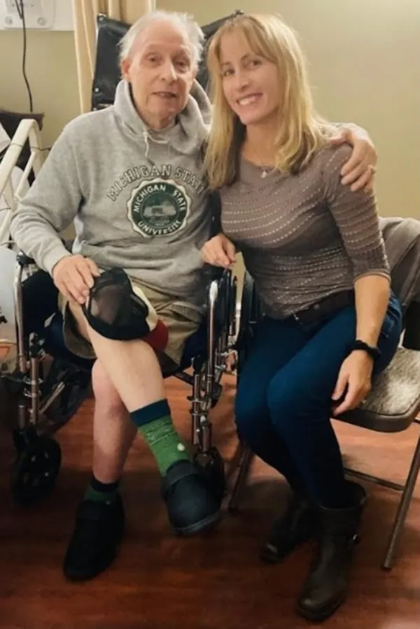 Laura with an elderly person two individuals sitting closely, one with a prosthetic leg and the other in jeans
