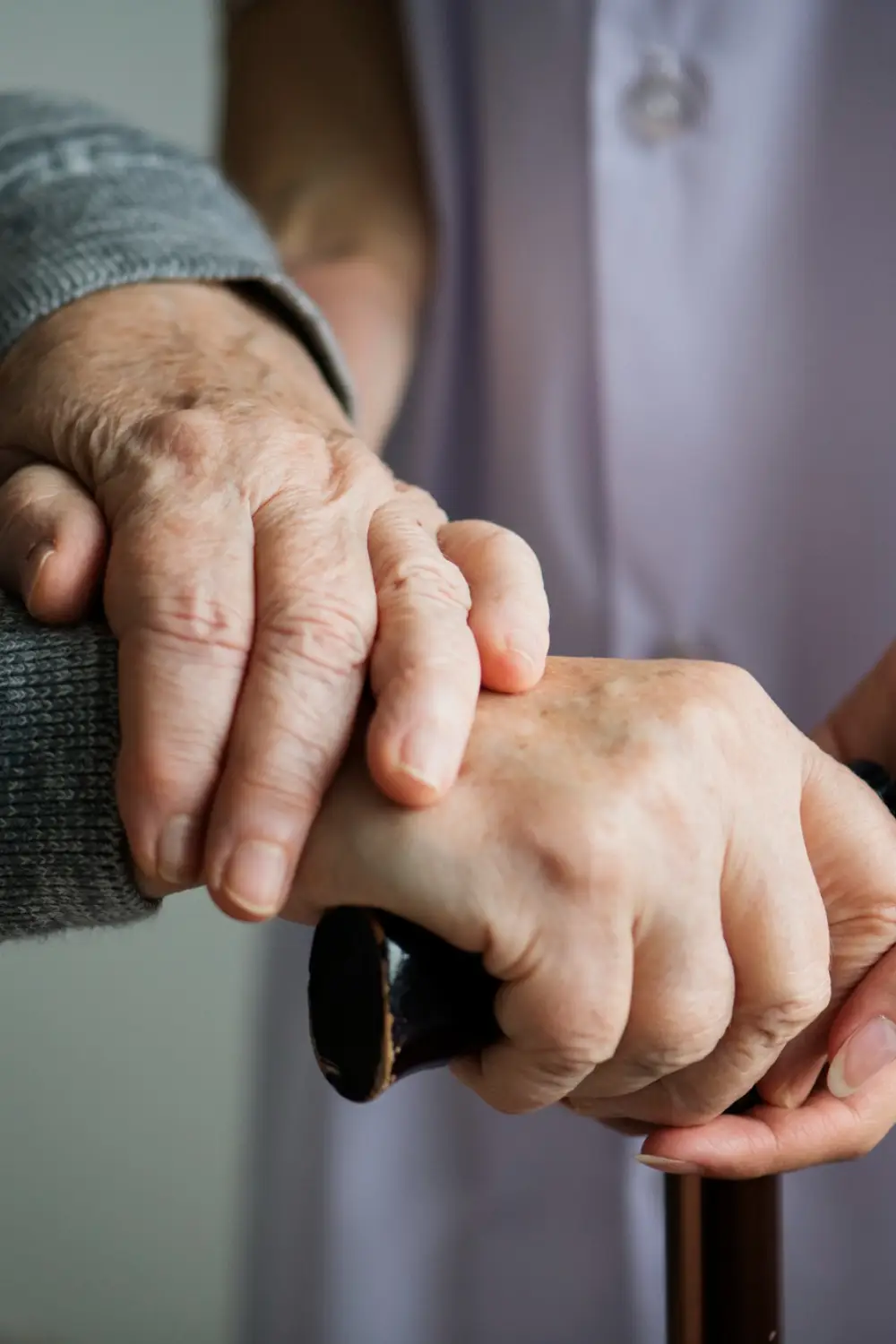A caregiver gently holds the hand of an elderly person, who is gripping a cane, symbolizing support and assistance A caregiver gently holds the hand of an elderly person, who is gripping a cane, symbolizing support and assistance